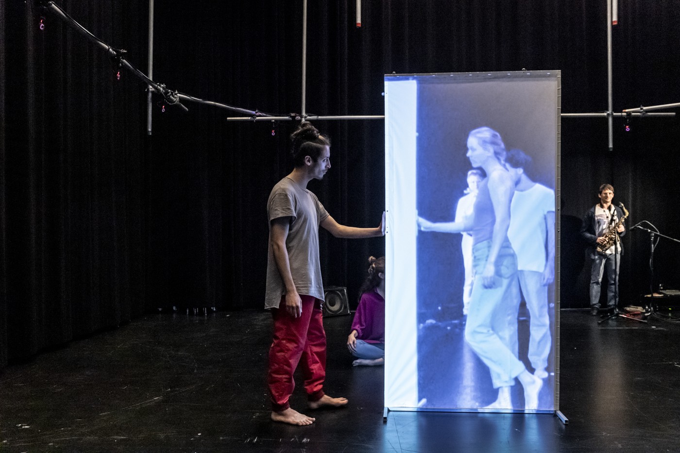 A dancer interacting with performers projected onto a mobile screen.