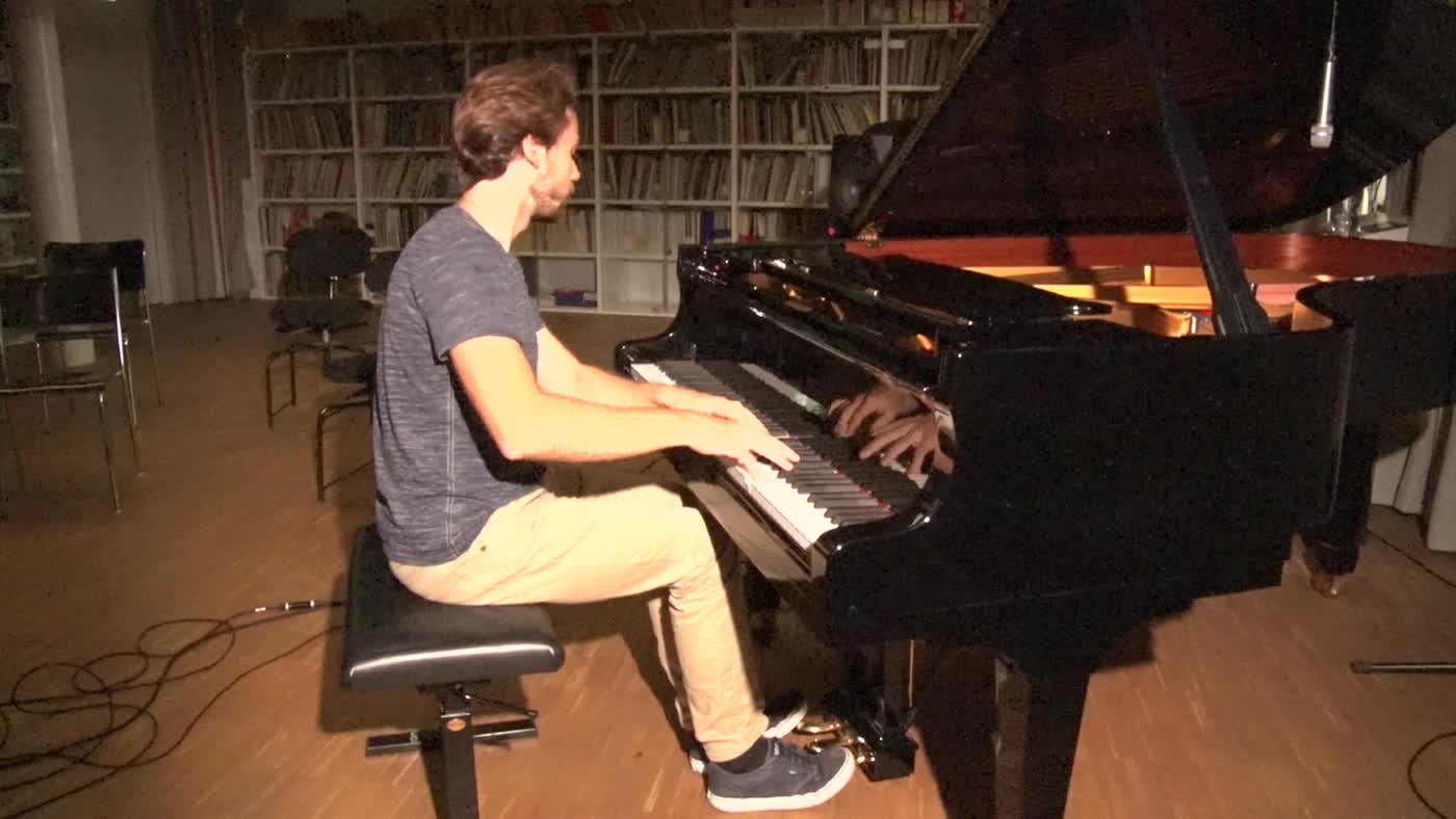 A pianist playing a grand piano in a room lined with bookshelves.