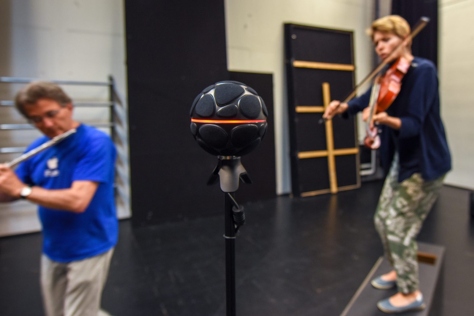 A flute player and a viola player on either side of the Zylia microphone; the viola player stands on a wooden platform.